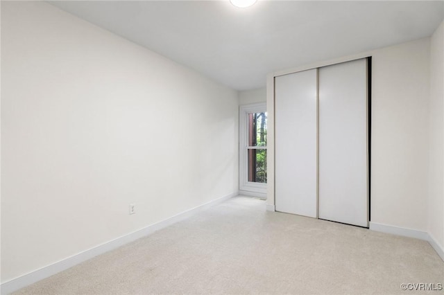 unfurnished bedroom with light colored carpet, a closet, and baseboards