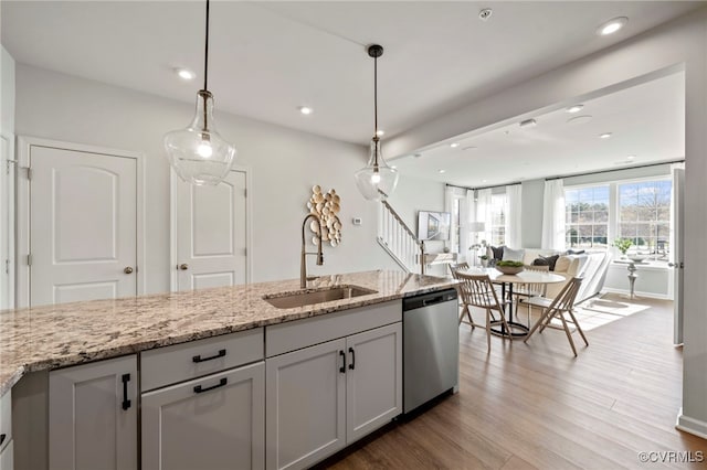 kitchen with stainless steel dishwasher, a sink, light wood-style floors, light stone counters, and pendant lighting