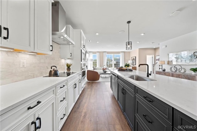 kitchen featuring a sink, wall chimney range hood, stainless steel appliances, white cabinets, and light countertops