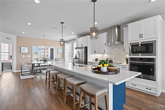 kitchen with appliances with stainless steel finishes, wall chimney range hood, a sink, light countertops, and decorative backsplash