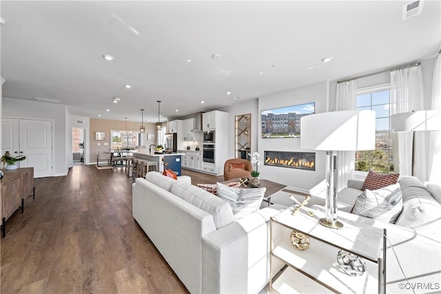 living room with a glass covered fireplace, dark wood finished floors, recessed lighting, and baseboards