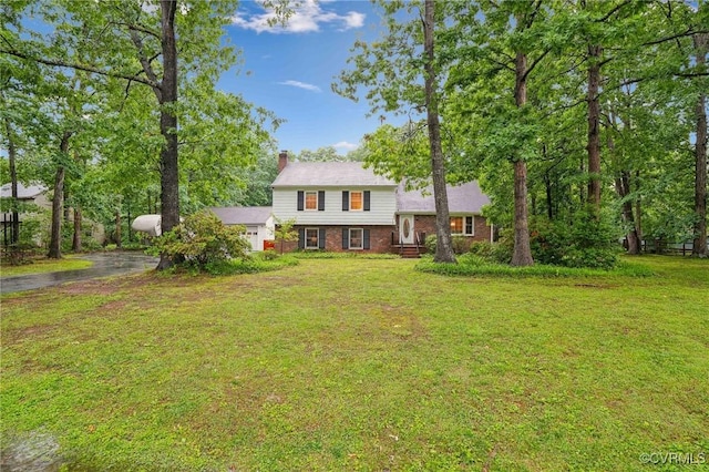 split level home featuring brick siding, a chimney, a front lawn, and asphalt driveway