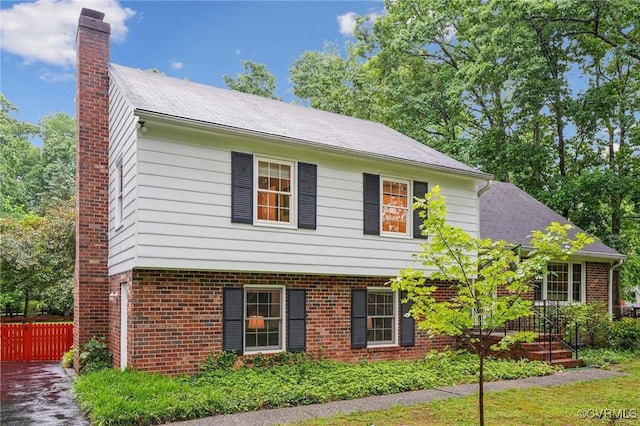 view of front of home featuring a chimney, brick siding, and fence