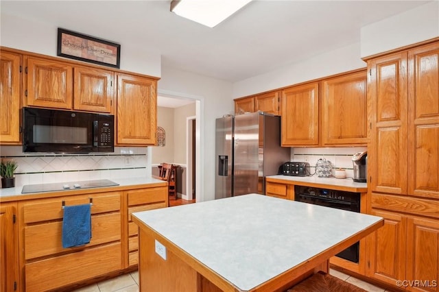 kitchen with black microwave, stainless steel fridge with ice dispenser, decorative backsplash, light countertops, and a kitchen island