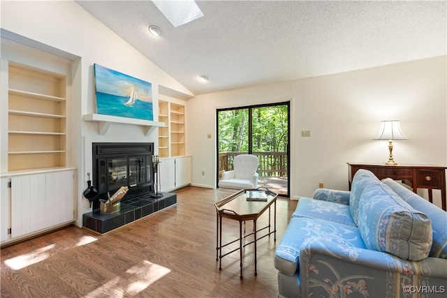 living area featuring vaulted ceiling, built in shelves, a textured ceiling, a skylight, and wood finished floors