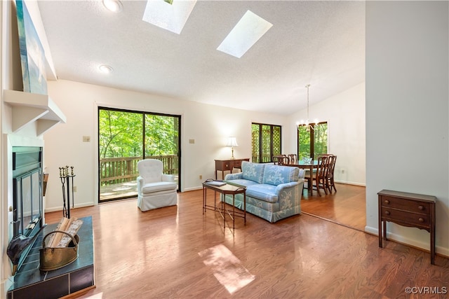 living room with vaulted ceiling, wood finished floors, a chandelier, a skylight, and baseboards