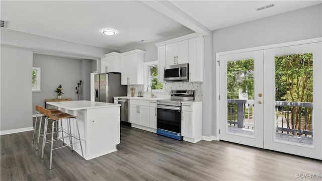 kitchen with stainless steel appliances, a sink, a kitchen island, a breakfast bar, and white cabinetry