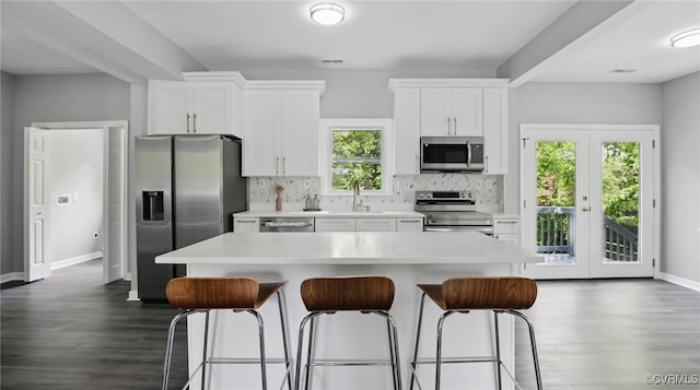 kitchen with stainless steel appliances, a kitchen breakfast bar, white cabinets, and dark wood-style floors