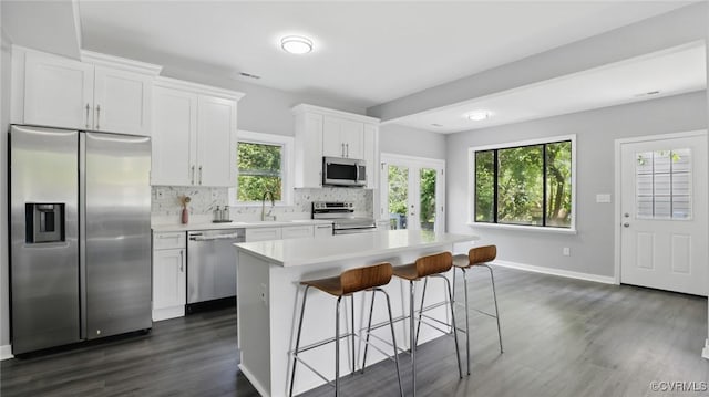 kitchen with appliances with stainless steel finishes, a sink, a center island, dark wood finished floors, and tasteful backsplash