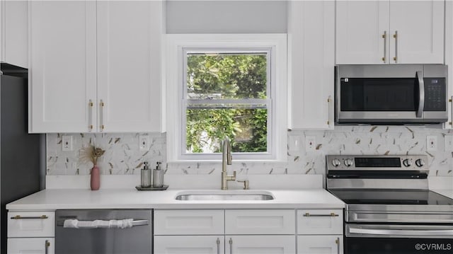 kitchen with stainless steel appliances, a sink, white cabinetry, light countertops, and decorative backsplash