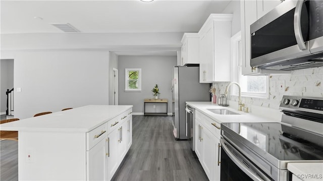 kitchen featuring appliances with stainless steel finishes, a sink, a kitchen island, decorative backsplash, and white cabinetry