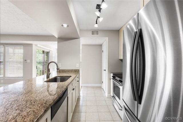 kitchen featuring appliances with stainless steel finishes, a sink, track lighting, light tile patterned flooring, and light stone counters
