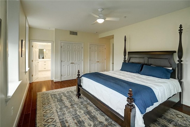 bedroom featuring two closets, wood finished floors, baseboards, ensuite bathroom, and ceiling fan