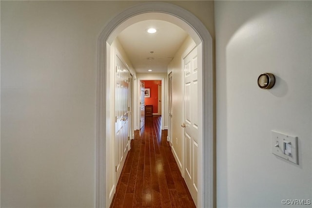 corridor featuring arched walkways, dark wood-style flooring, recessed lighting, and baseboards