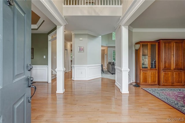 foyer with decorative columns, ornamental molding, light wood finished floors, a decorative wall, and a wainscoted wall