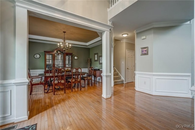 dining space with light wood finished floors, stairway, ornamental molding, a chandelier, and a wainscoted wall