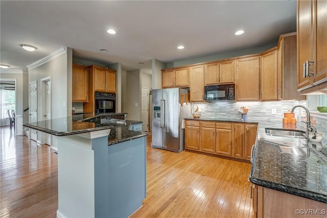 kitchen with black appliances, a sink, crown molding, dark stone countertops, and light wood-style floors