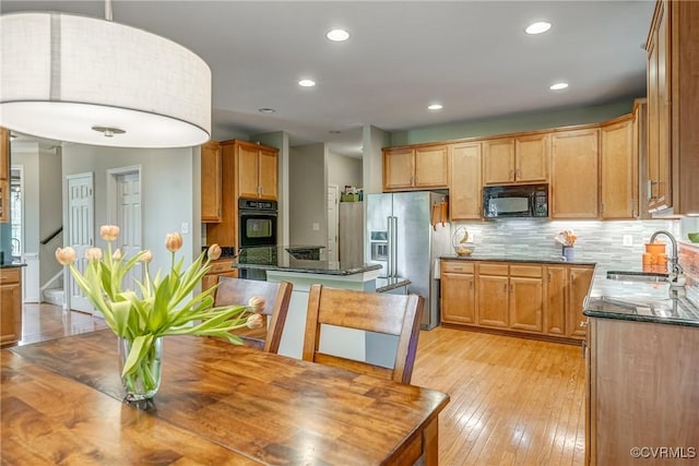 kitchen with a sink, black appliances, tasteful backsplash, light wood-style flooring, and recessed lighting