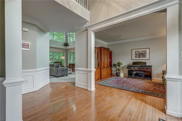foyer featuring decorative columns, light wood finished floors, crown molding, and wainscoting