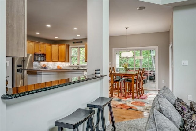 kitchen featuring black microwave, high quality fridge, light wood finished floors, recessed lighting, and decorative backsplash