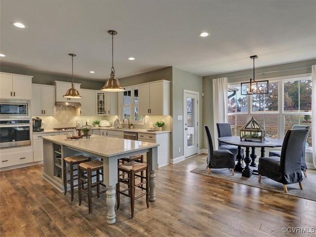 kitchen featuring stainless steel appliances, a chandelier, a breakfast bar area, decorative backsplash, and white cabinetry