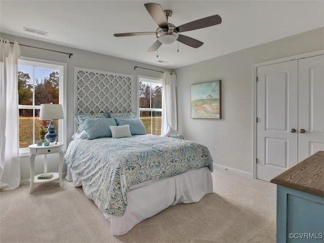 bedroom with light colored carpet, multiple windows, baseboards, and a ceiling fan