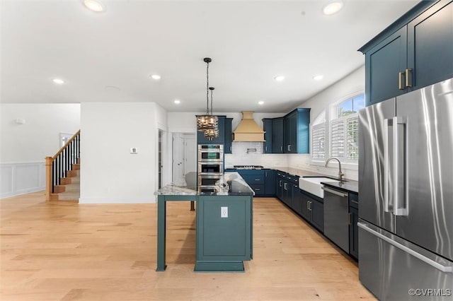 kitchen featuring appliances with stainless steel finishes, a sink, light wood finished floors, custom exhaust hood, and a center island