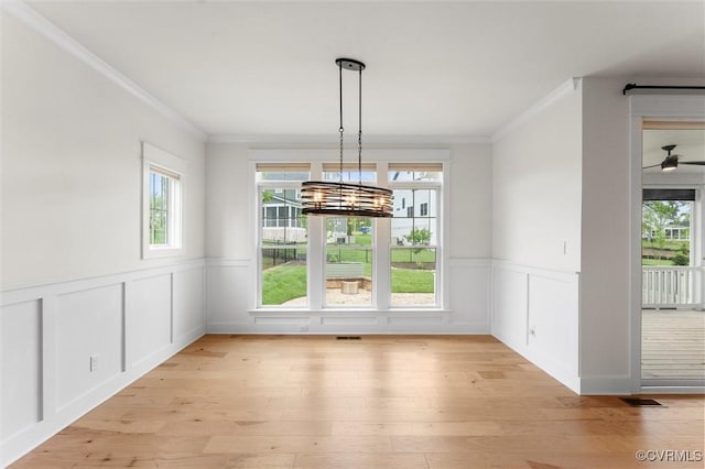 unfurnished dining area with crown molding, light wood finished floors, wainscoting, a decorative wall, and a chandelier