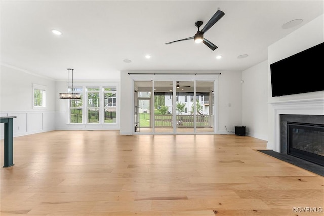 unfurnished living room with a fireplace with flush hearth, ceiling fan, light wood finished floors, recessed lighting, and a wainscoted wall