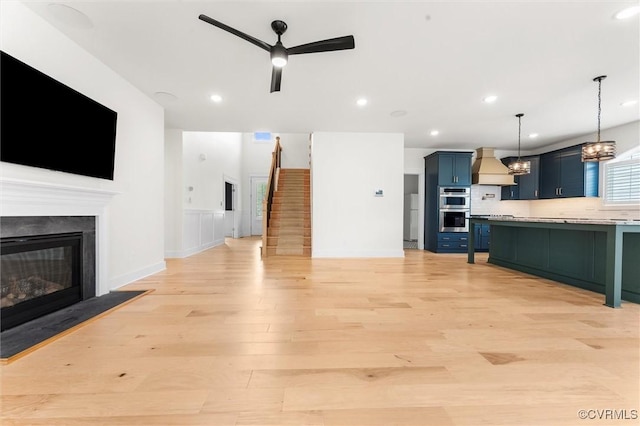 living room with a ceiling fan, light wood-style floors, a glass covered fireplace, stairs, and recessed lighting
