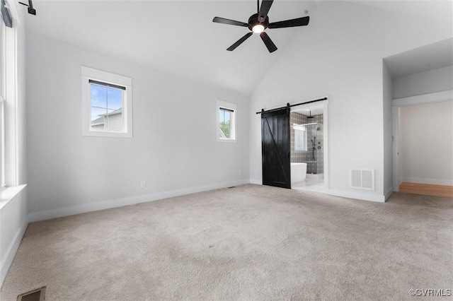unfurnished bedroom featuring a barn door, high vaulted ceiling, carpet floors, baseboards, and connected bathroom