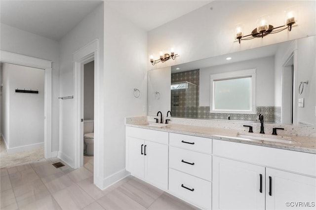 bathroom with a stall shower, toilet, double vanity, and baseboards