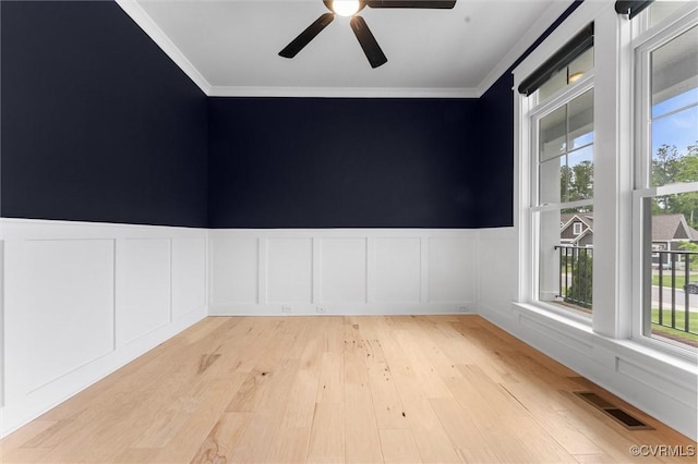 unfurnished room with ornamental molding, a ceiling fan, a decorative wall, light wood-style flooring, and a wainscoted wall