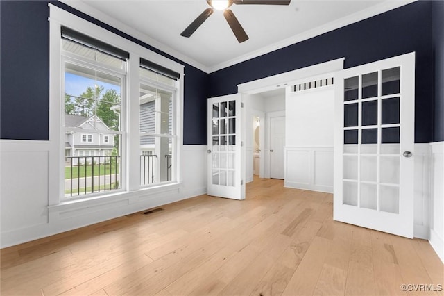 unfurnished room with a decorative wall, a ceiling fan, wainscoting, light wood-type flooring, and crown molding