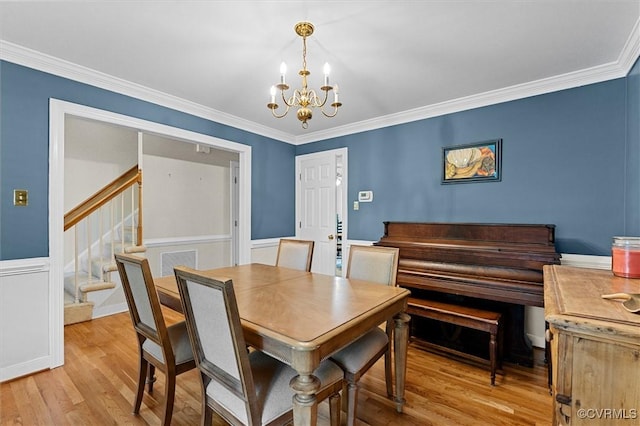 dining space featuring a chandelier, light wood-style floors, crown molding, and stairs