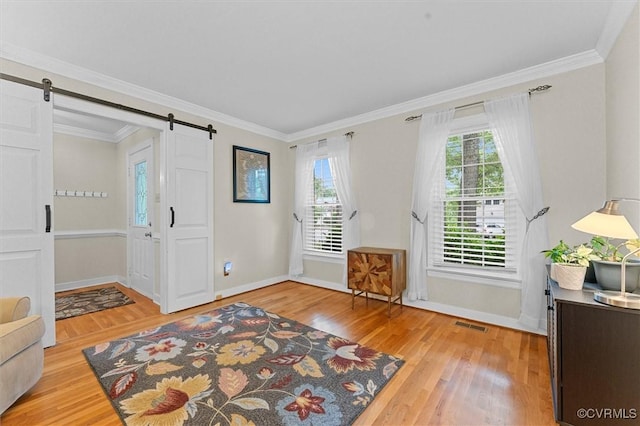 foyer entrance with a barn door, light wood-style floors, crown molding, and baseboards
