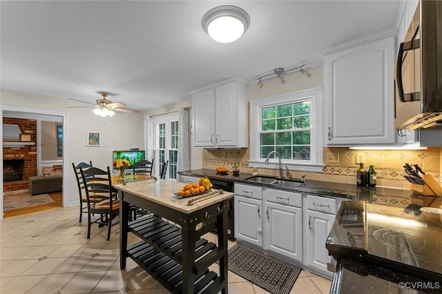 kitchen with a sink, decorative backsplash, light tile patterned floors, a ceiling fan, and white cabinets
