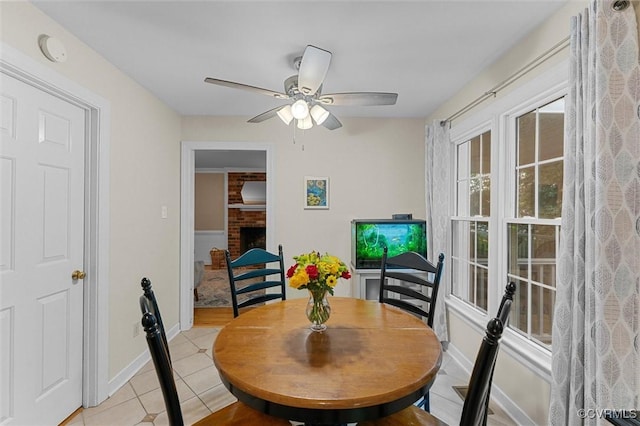 dining area featuring light tile patterned floors, ceiling fan, a brick fireplace, and baseboards