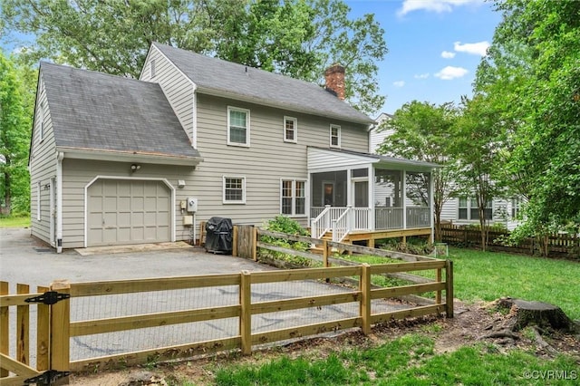 back of property featuring a chimney, a sunroom, asphalt driveway, an attached garage, and roof with shingles
