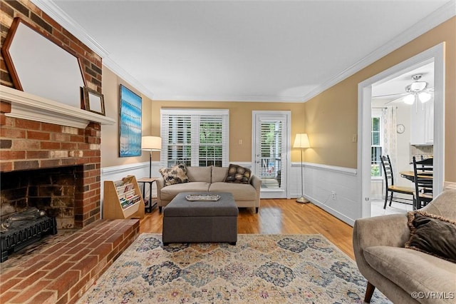 living area featuring crown molding, a wainscoted wall, plenty of natural light, a fireplace, and wood finished floors