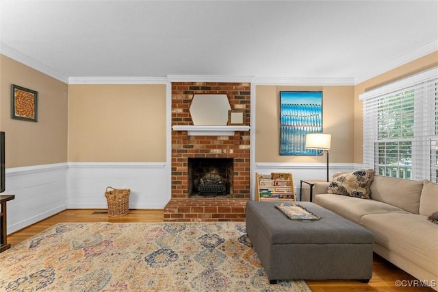 living room with ornamental molding, a brick fireplace, wood finished floors, and wainscoting