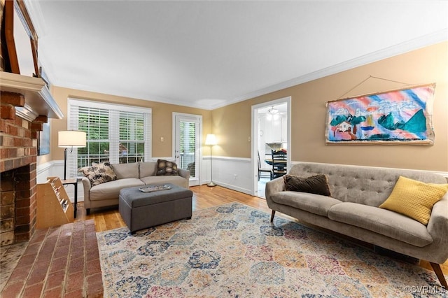 living area with ornamental molding, a wainscoted wall, wood finished floors, a fireplace, and a ceiling fan
