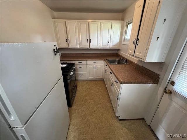kitchen with freestanding refrigerator, stainless steel range with gas stovetop, a sink, white cabinets, and dark countertops