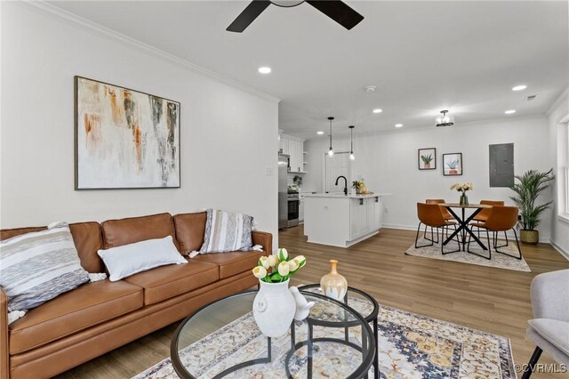 living area featuring recessed lighting, a ceiling fan, ornamental molding, light wood finished floors, and electric panel