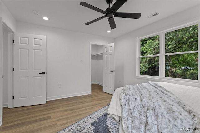 bedroom featuring wood finished floors, recessed lighting, baseboards, ceiling fan, and a walk in closet