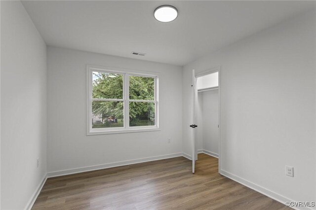 unfurnished bedroom with wood finished floors, baseboards, a closet, and a walk in closet