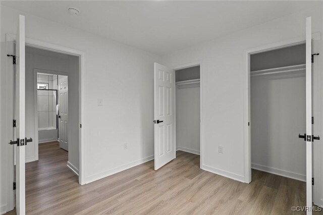 unfurnished bedroom with two closets, light wood-type flooring, and baseboards