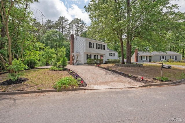 view of front of house with asphalt driveway, a chimney, and view of scattered trees