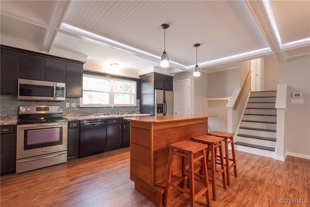 kitchen with appliances with stainless steel finishes, tasteful backsplash, a breakfast bar, wood finished floors, and a center island