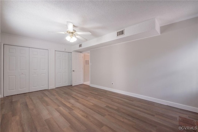 unfurnished bedroom featuring two closets, baseboards, wood finished floors, a textured ceiling, and ceiling fan